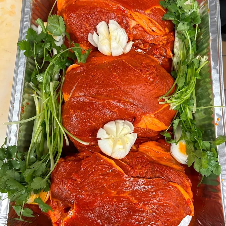 Marinated red meat cuts with garlic and cilantro in a foil pan, ready for cooking.