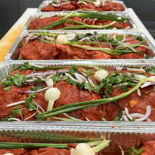 Marinated carne asada with onions, cilantro, and green onions in aluminum trays.