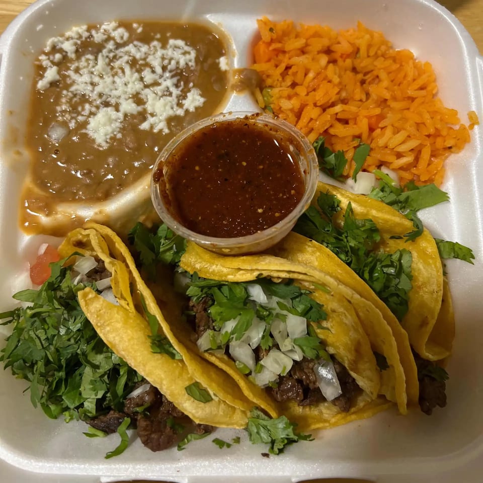 Three Los 4 Vientos Carniceria tacos with rice, beans, and salsa in a white takeout container.