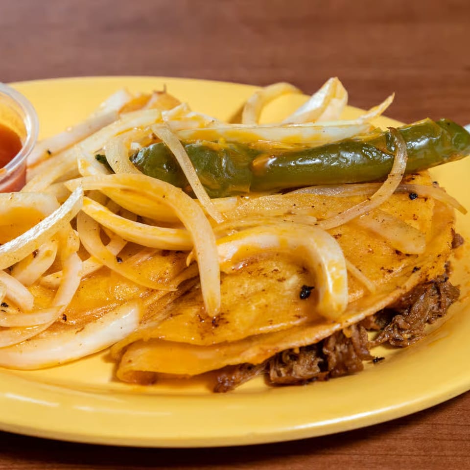 A Los 4 Vientos Carniceria Mexican taco with meat, onions, and a green chili on a yellow plate.