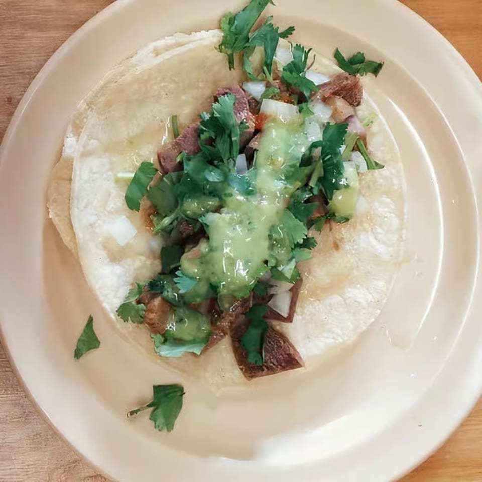 Overhead view of a Los 4 Vientos Carniceria taco with meat, onions, cilantro, and green sauce.