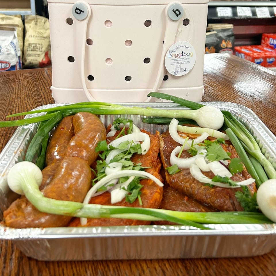 Mexican chorizo and marinated meat with green onions, white onions, and cilantro in a foil tray.